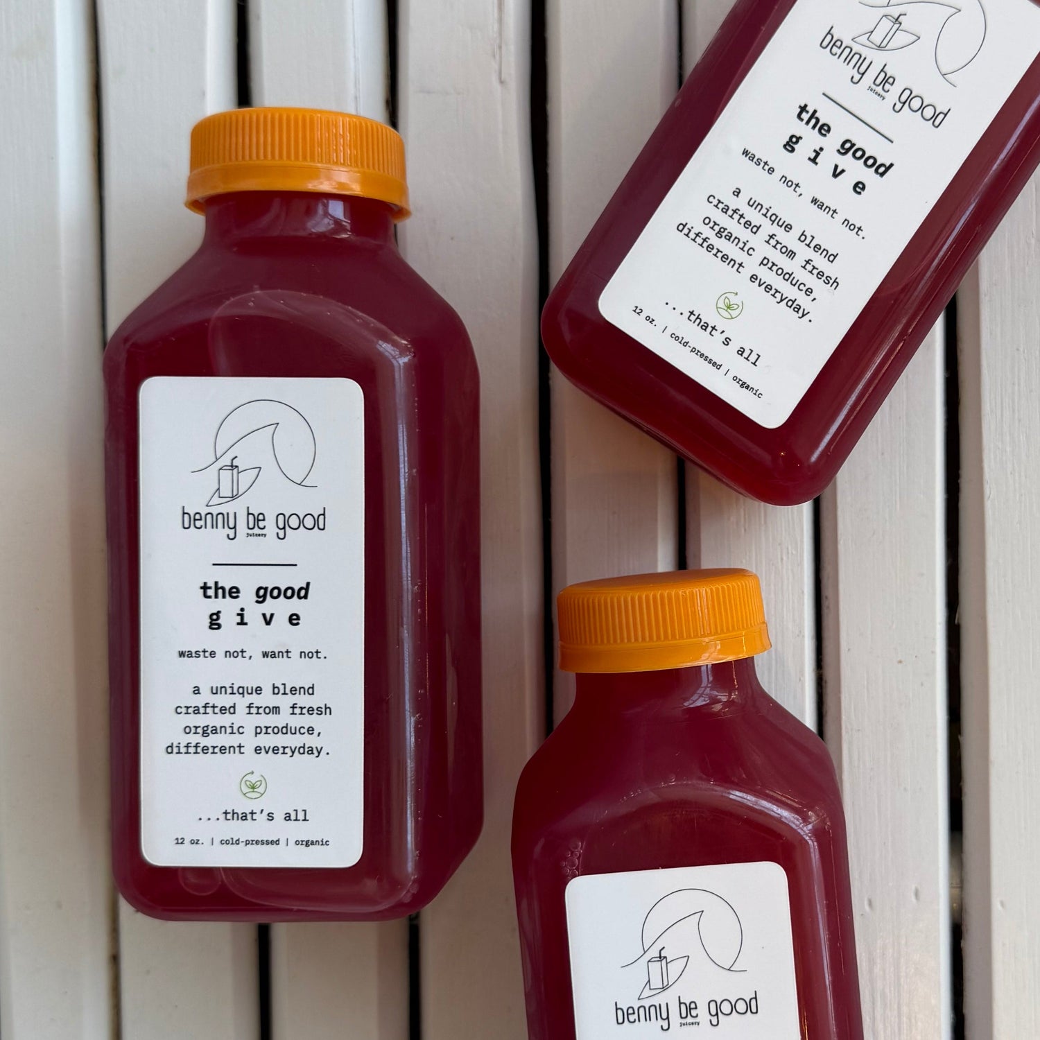 Three bottles of our good give juice with labels on a wooden surface