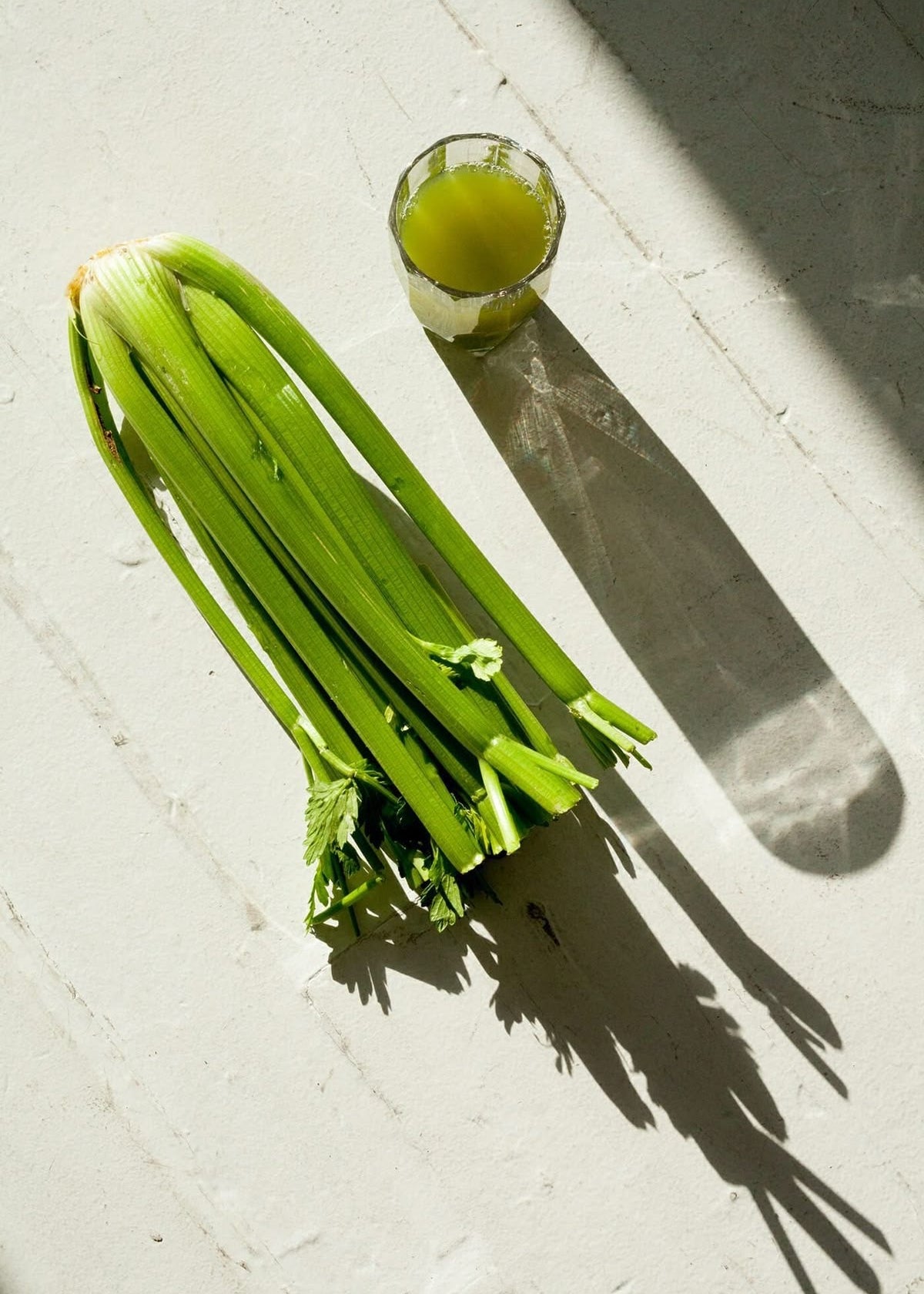 Bunch of celery and a glass of juice on a light surface